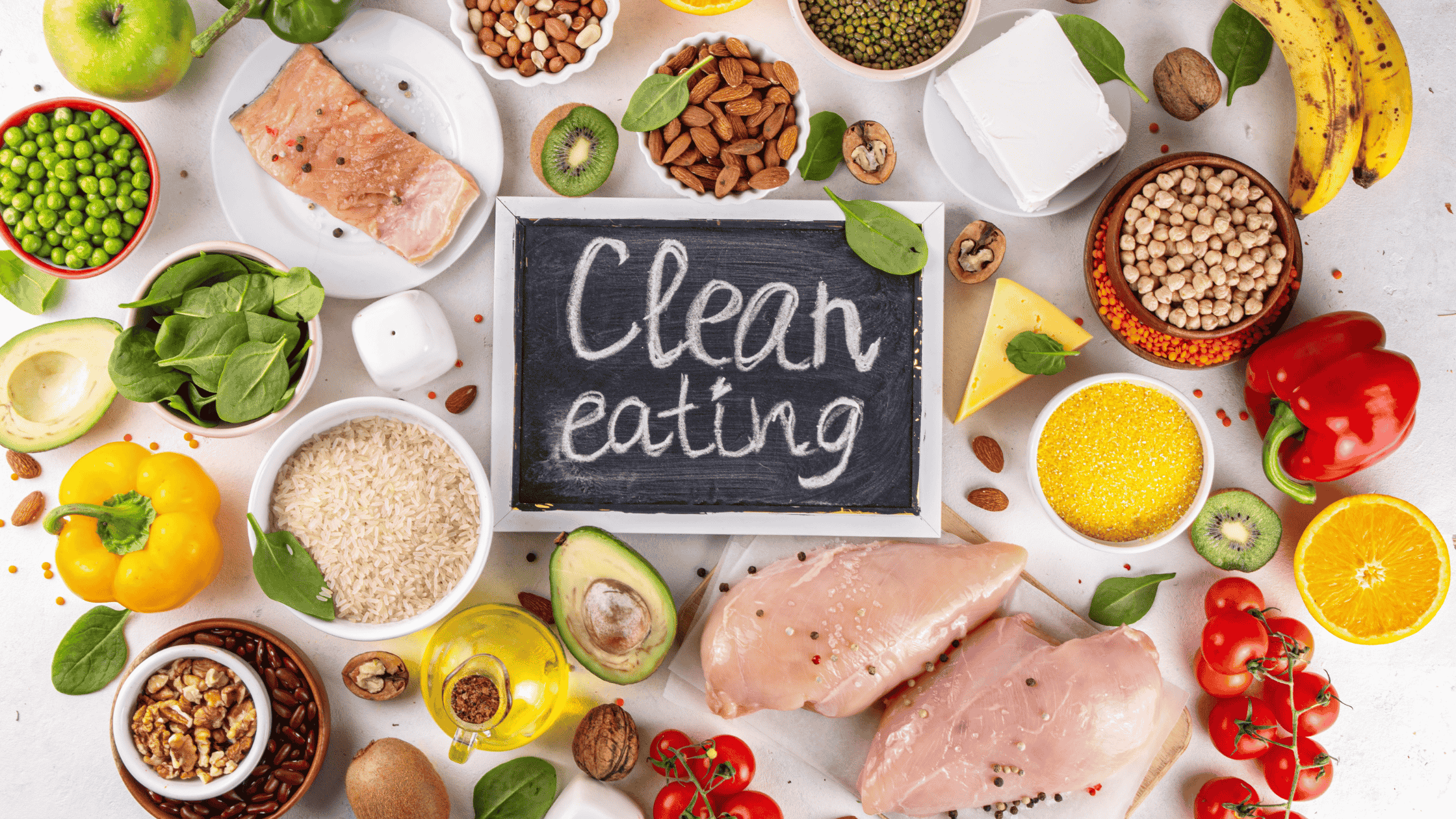 The words "clean eating" on a mini chalkboard with a variety of whole foods surrounding it.