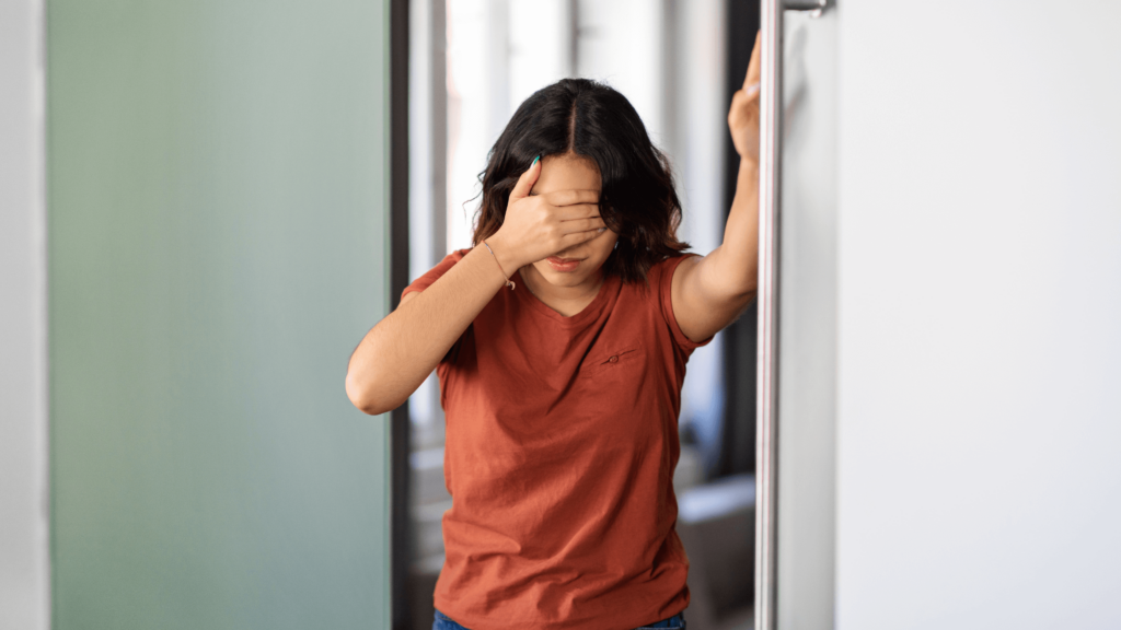 Woman Wearing red shirt, holding a hand over her eyes, like she has a headache.