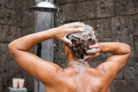 Close up of upper shoulders and head. Person in shower lathering shampoo on scalp.