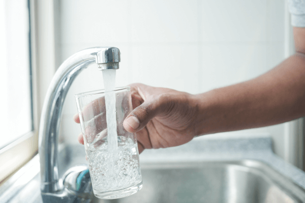 Hand with glass, filling water from faucet.