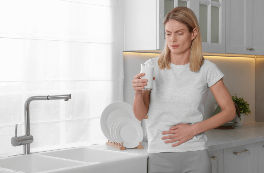 Woman wearing a white shirt, holding a glass of milk and clutching her stomach.