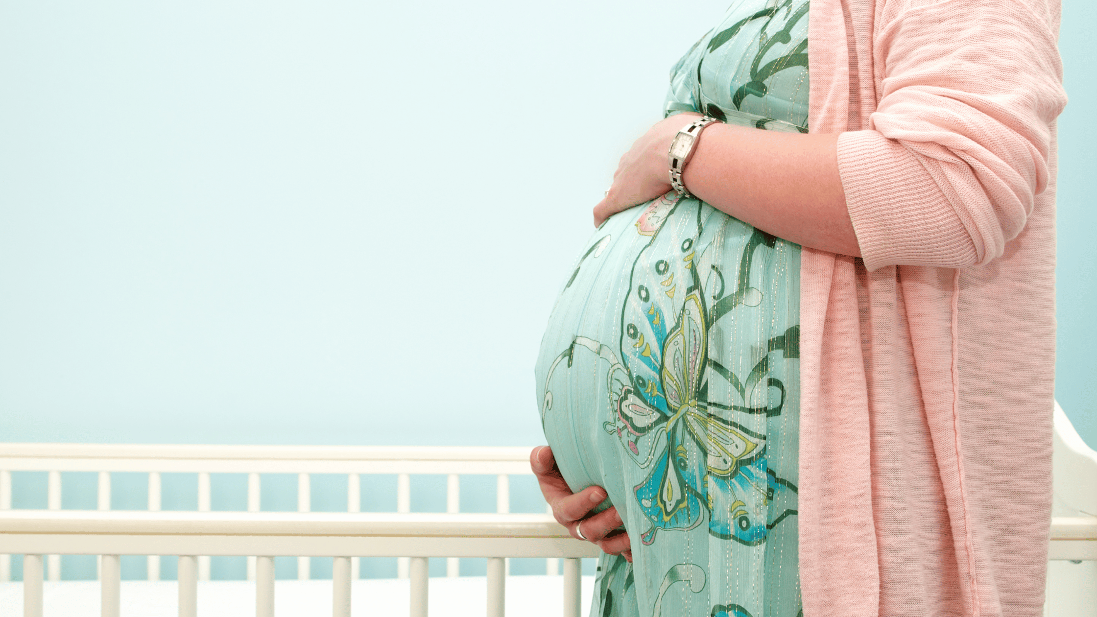 woman holding stomach in pregnancy with mint green background and matching dress