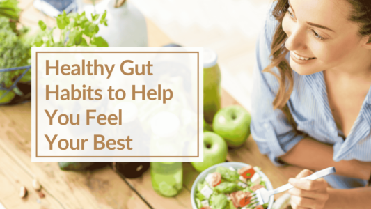 A woman wearing a blue shirt is leaning at a table, she is eating a salad and is surrounded by healthy food like apples, juice and other vegetables. Text Overlay: Healthy Gut Habits to Help You Feel Your Best
