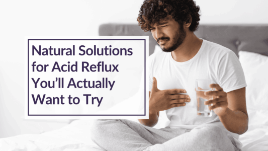 A man sitting on a bed with a glass of water in one hand and he is clutching his chest in pain in the other. Text Overlay: Natural Solutions for Acid Reflux You'll Actually Want to Try