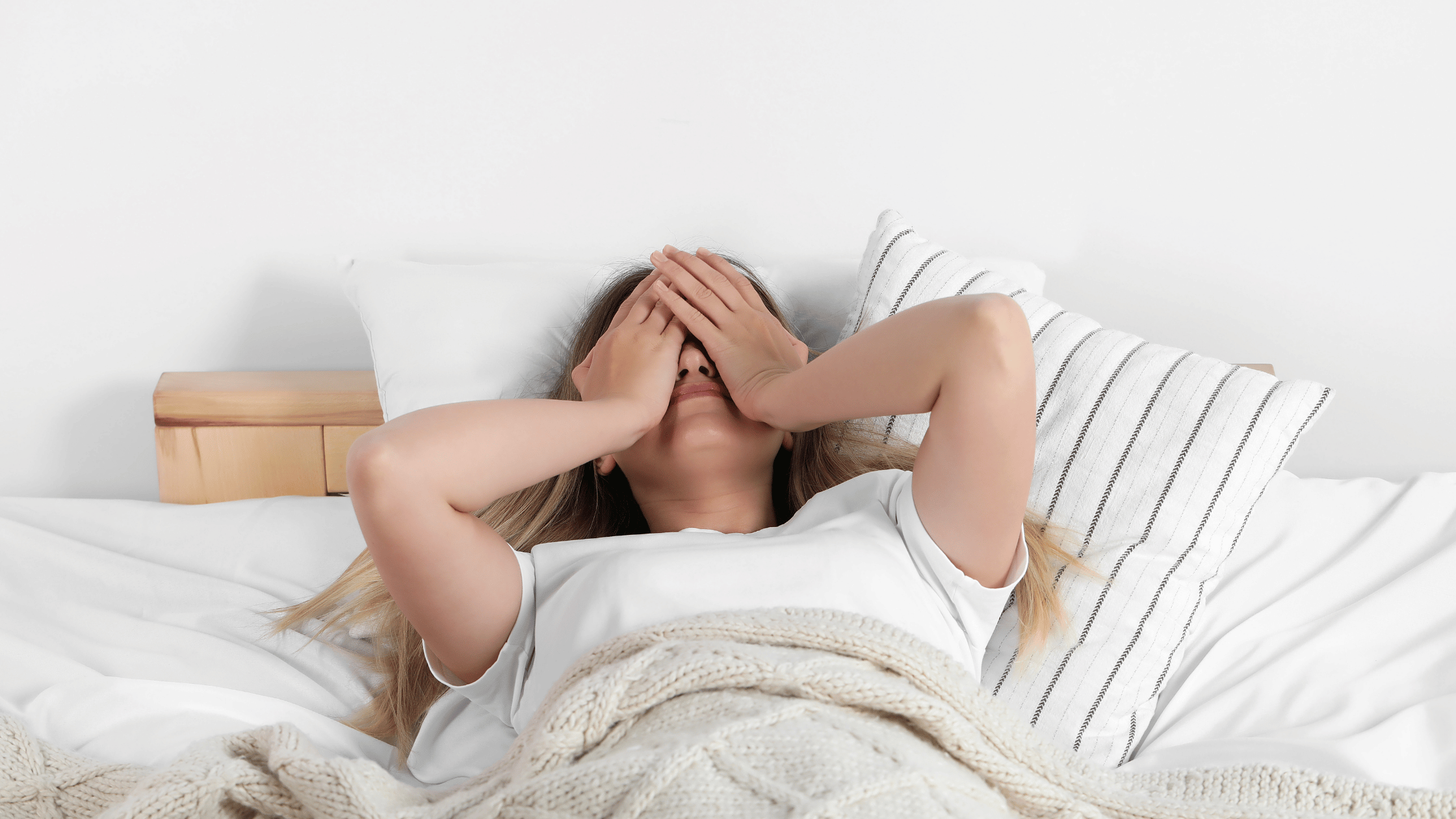 A woman in bed with hands over face. Denotes chronic fatigue.