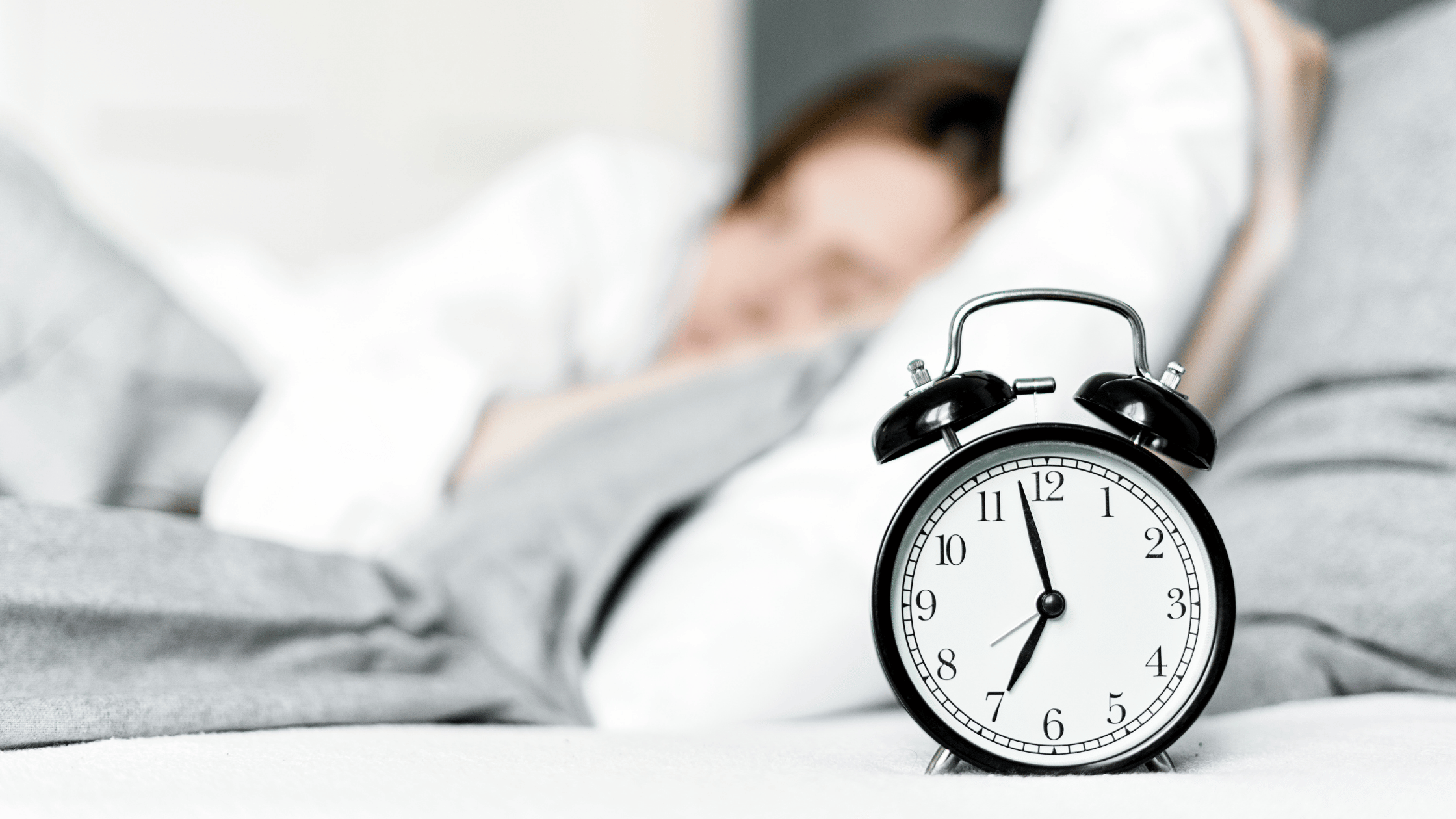 close up of an alarm clock, and a blurred image of a person sleeping.